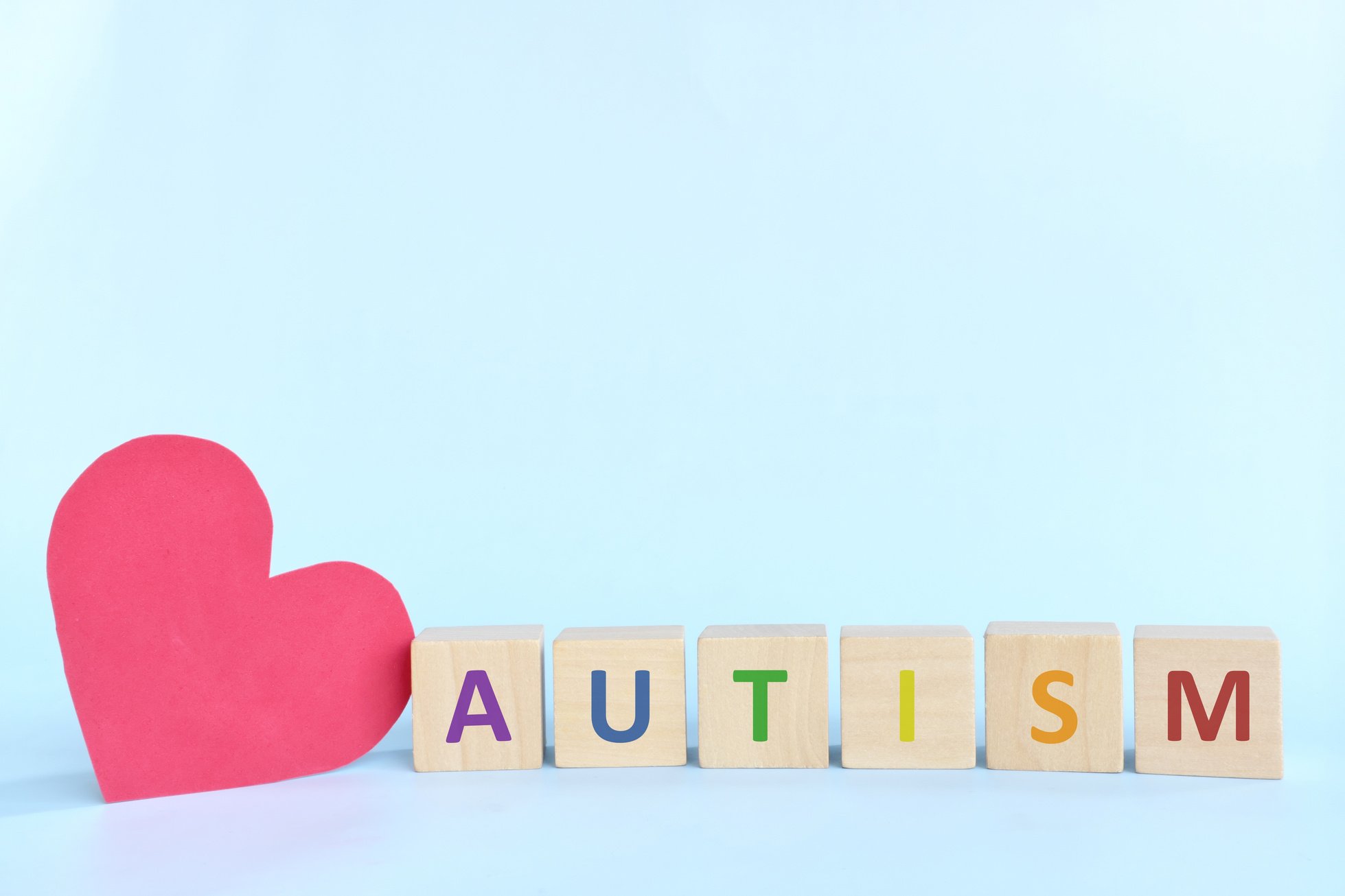 Big red heart shape beside autism letters in wooden blocks typography. Love, support autism spectrum disorder patient.